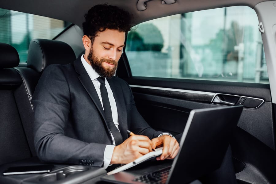 A passenger working on a laptop in the back seat